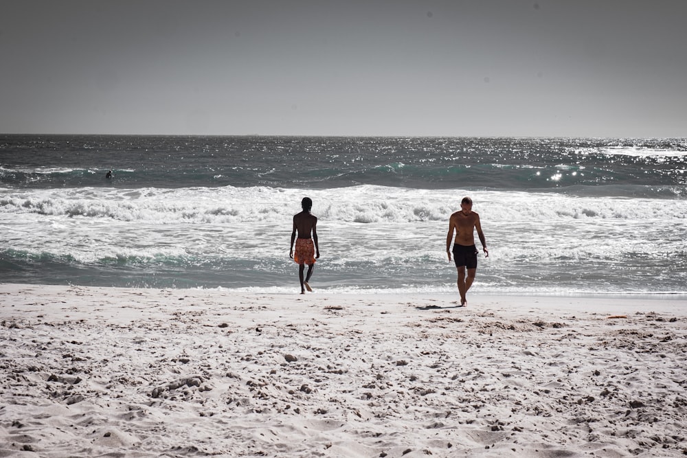two people walking on a beach near the ocean
