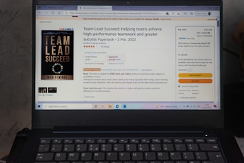 A laptop displays an Amazon product page for the book 'Team Lead Succeed'. The book cover is visible on the left, highlighting the title in bold letters. The page shows options to purchase in paperback or Kindle format, with price details and shipping options. The background includes a promotional message and a quote from the book.