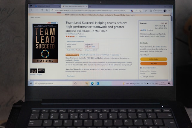 A laptop displays an Amazon product page for the book 'Team Lead Succeed'. The book cover is visible on the left, highlighting the title in bold letters. The page shows options to purchase in paperback or Kindle format, with price details and shipping options. The background includes a promotional message and a quote from the book.