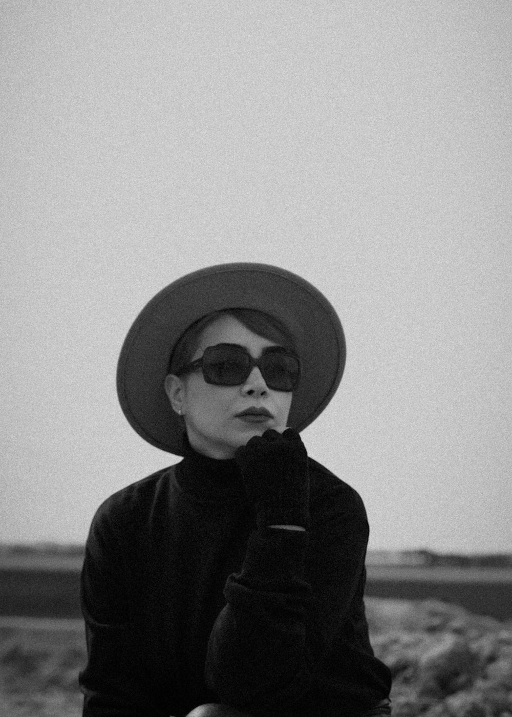 a woman wearing a hat and sunglasses sitting on a rock