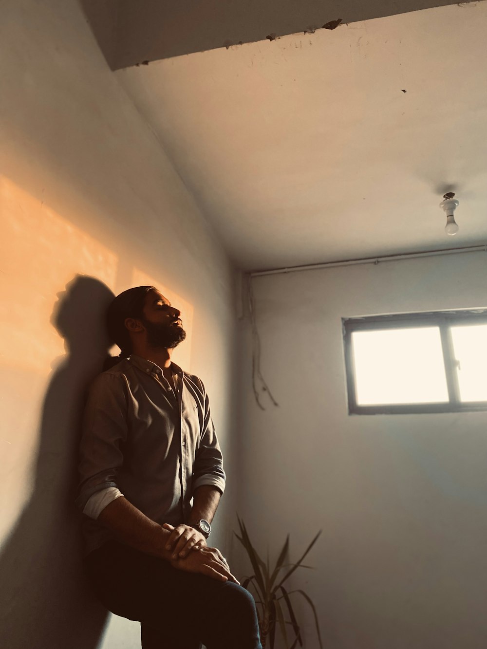 a man sitting against a wall next to a window