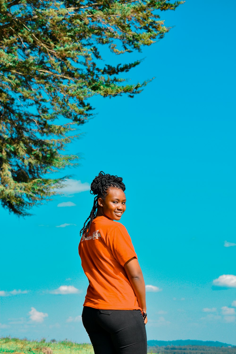 a woman in an orange shirt standing next to a tree