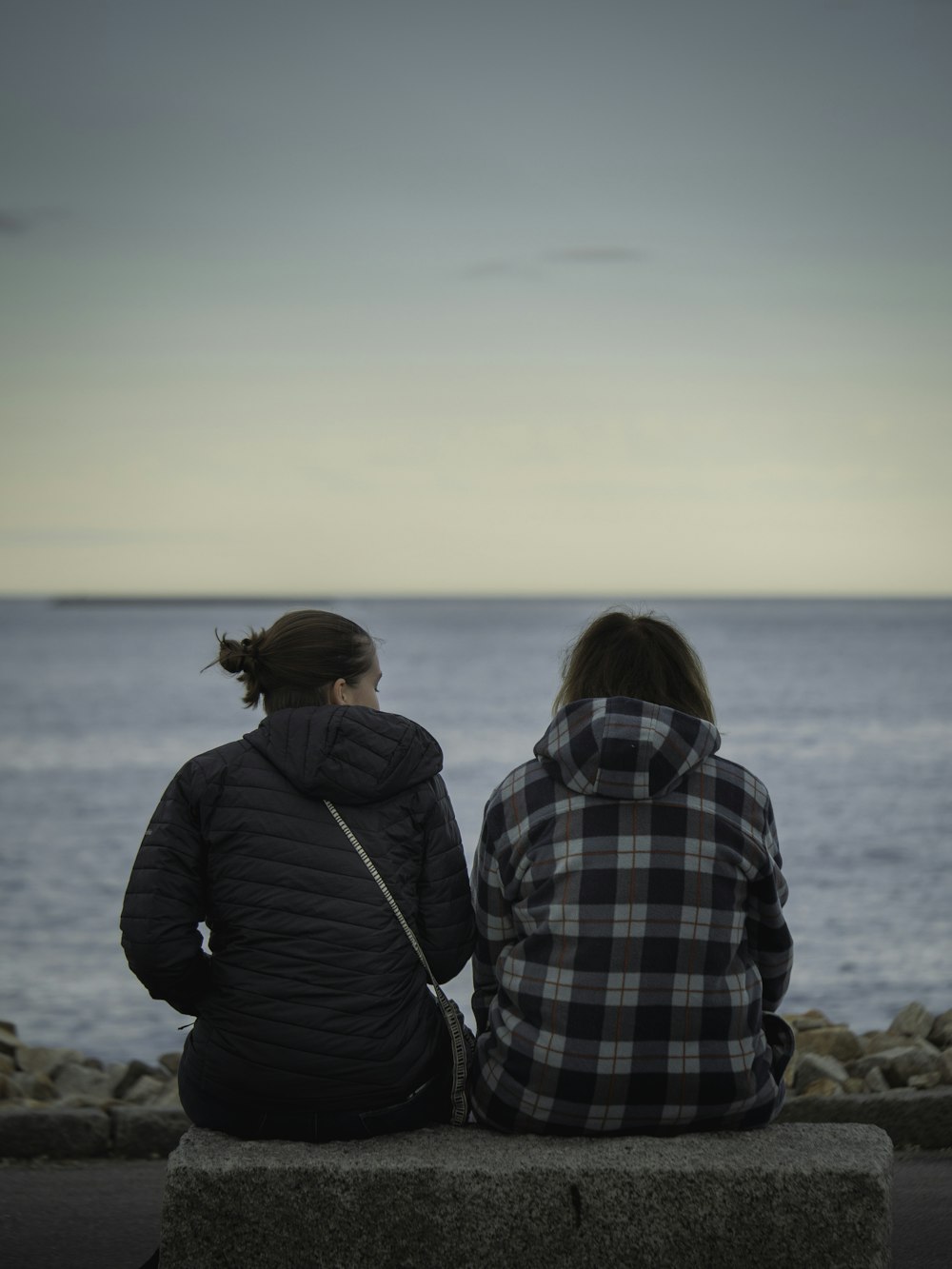 two people sitting on a bench looking out at the ocean