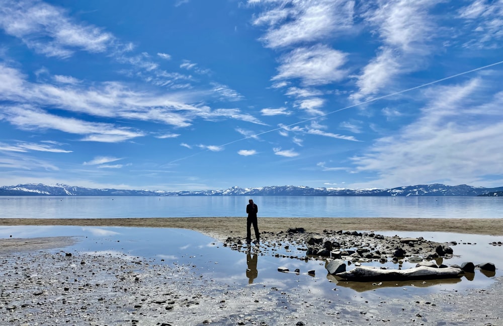 a man standing on a beach next to a body of water