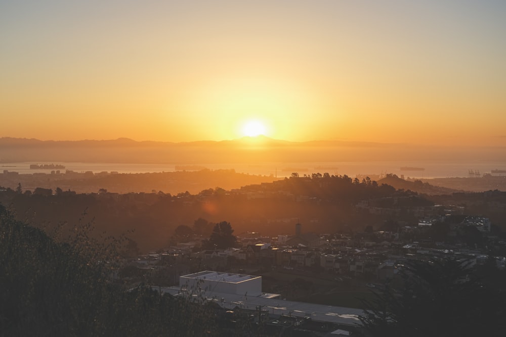 the sun is setting over a city with mountains in the background