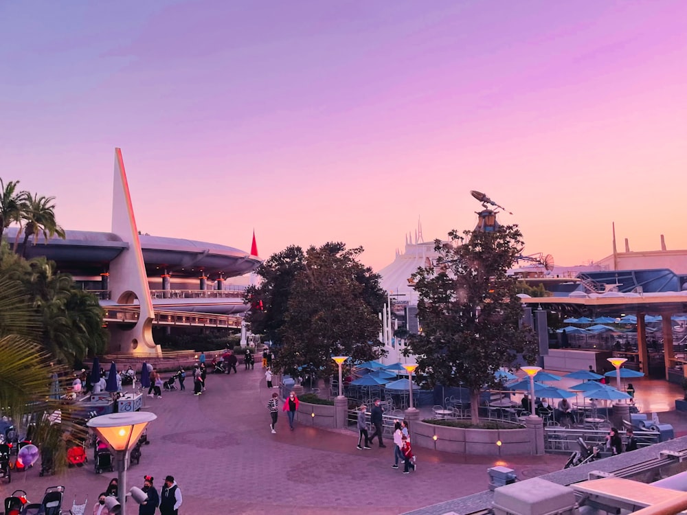 a crowd of people walking around a park at sunset