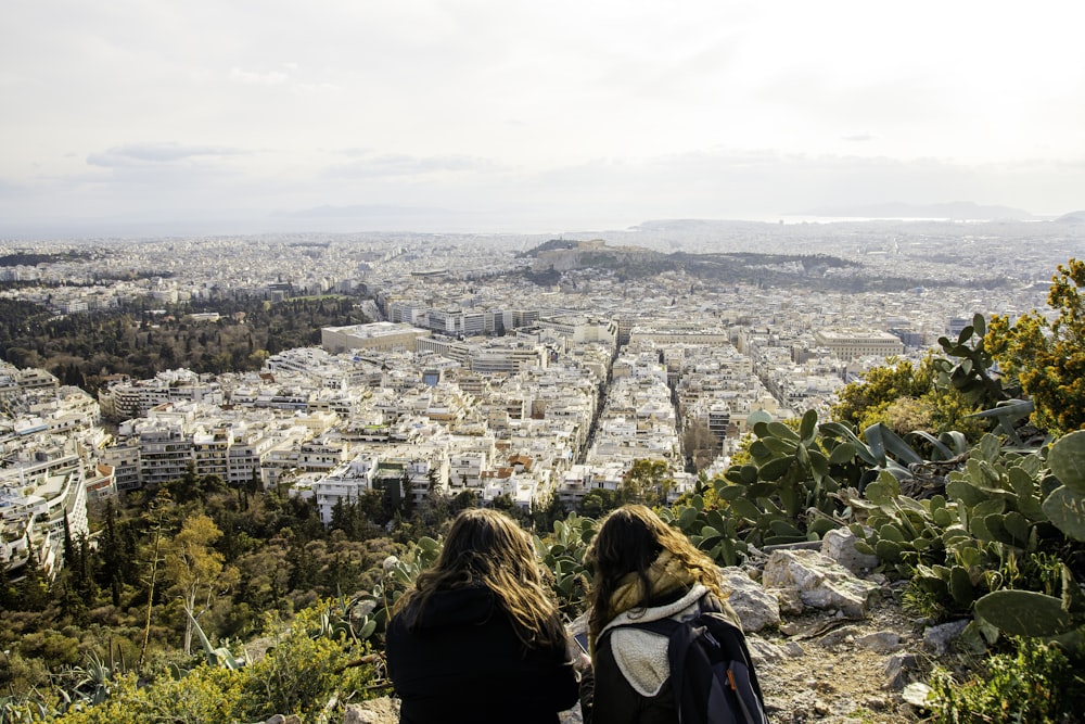 two women sitting on a hill overlooking a city