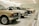 A row of classic cars displayed in a spacious showroom with a sleek, modern design. The cars vary in color and model, featuring vintage designs and pristine conditions, indicating a curated collection.