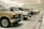 A row of classic cars displayed in a spacious showroom with a sleek, modern design. The cars vary in color and model, featuring vintage designs and pristine conditions, indicating a curated collection.