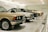 A row of classic cars displayed in a spacious showroom with a sleek, modern design. The cars vary in color and model, featuring vintage designs and pristine conditions, indicating a curated collection.