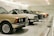 A row of classic cars displayed in a spacious showroom with a sleek, modern design. The cars vary in color and model, featuring vintage designs and pristine conditions, indicating a curated collection.