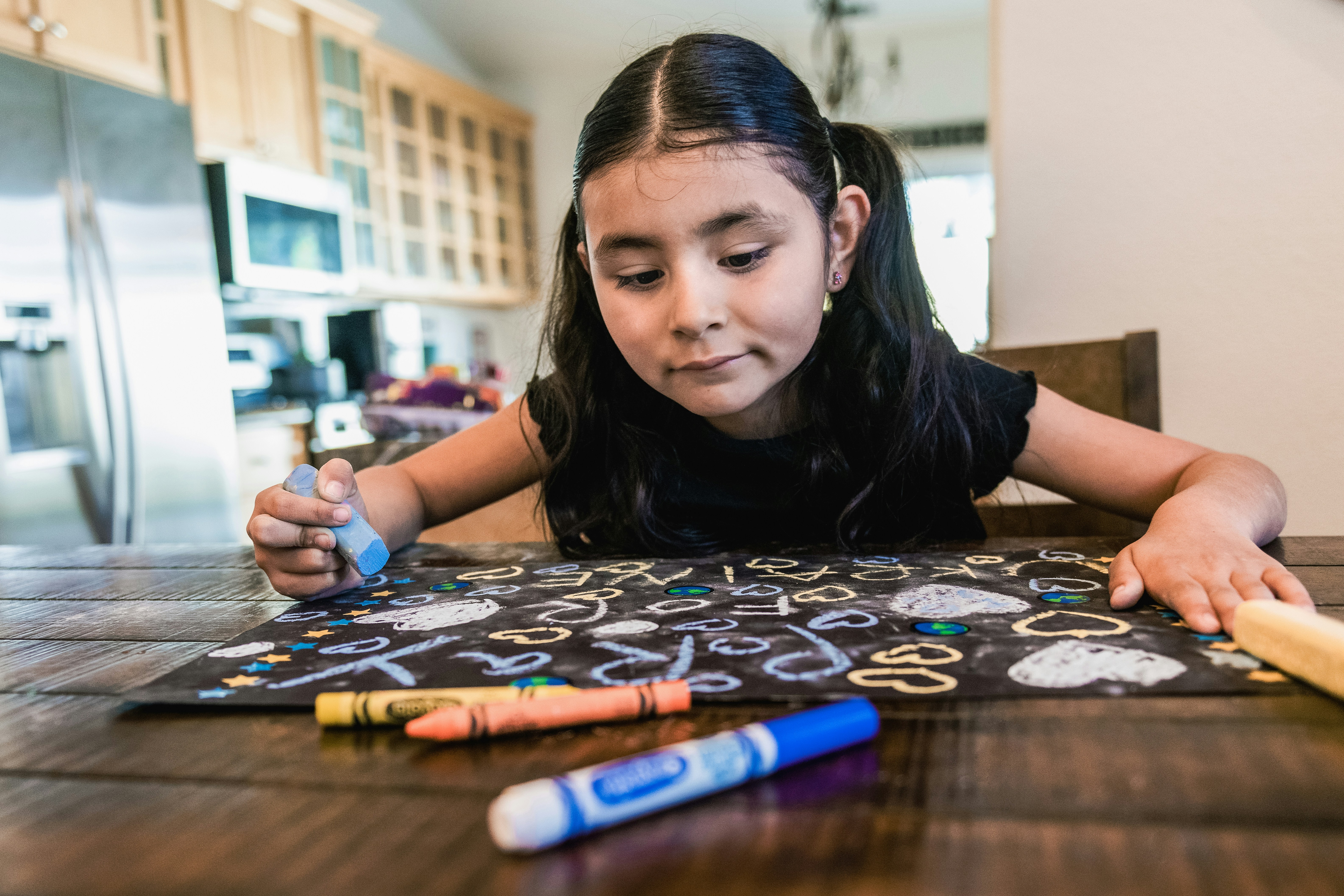a young girl sitting at a table drawing with crayons