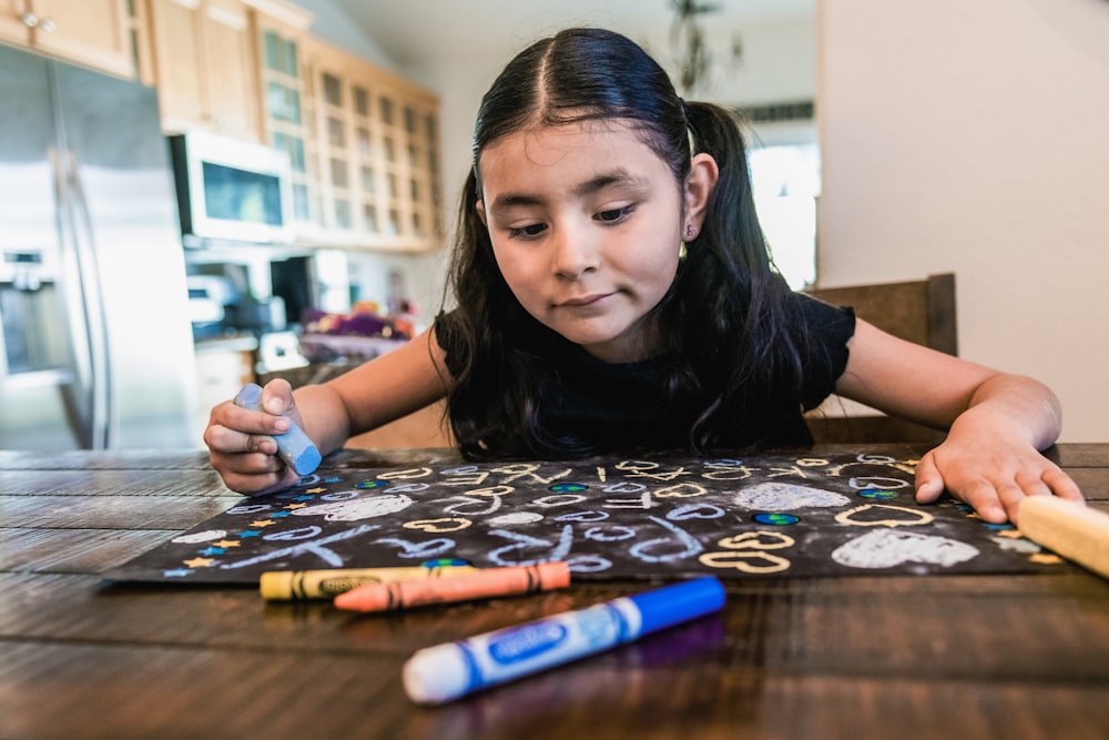 a young girl sitting at a table drawing with crayons