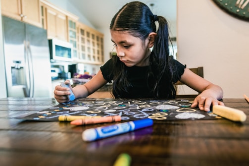 a little girl sitting at a table with crayons