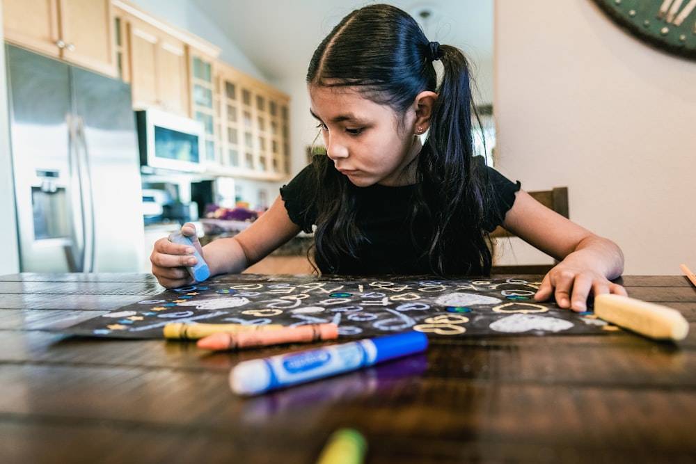 a little girl sitting at a table with crayons