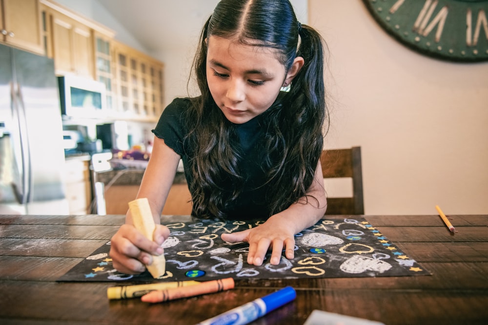 a young girl sitting at a table drawing with crayons