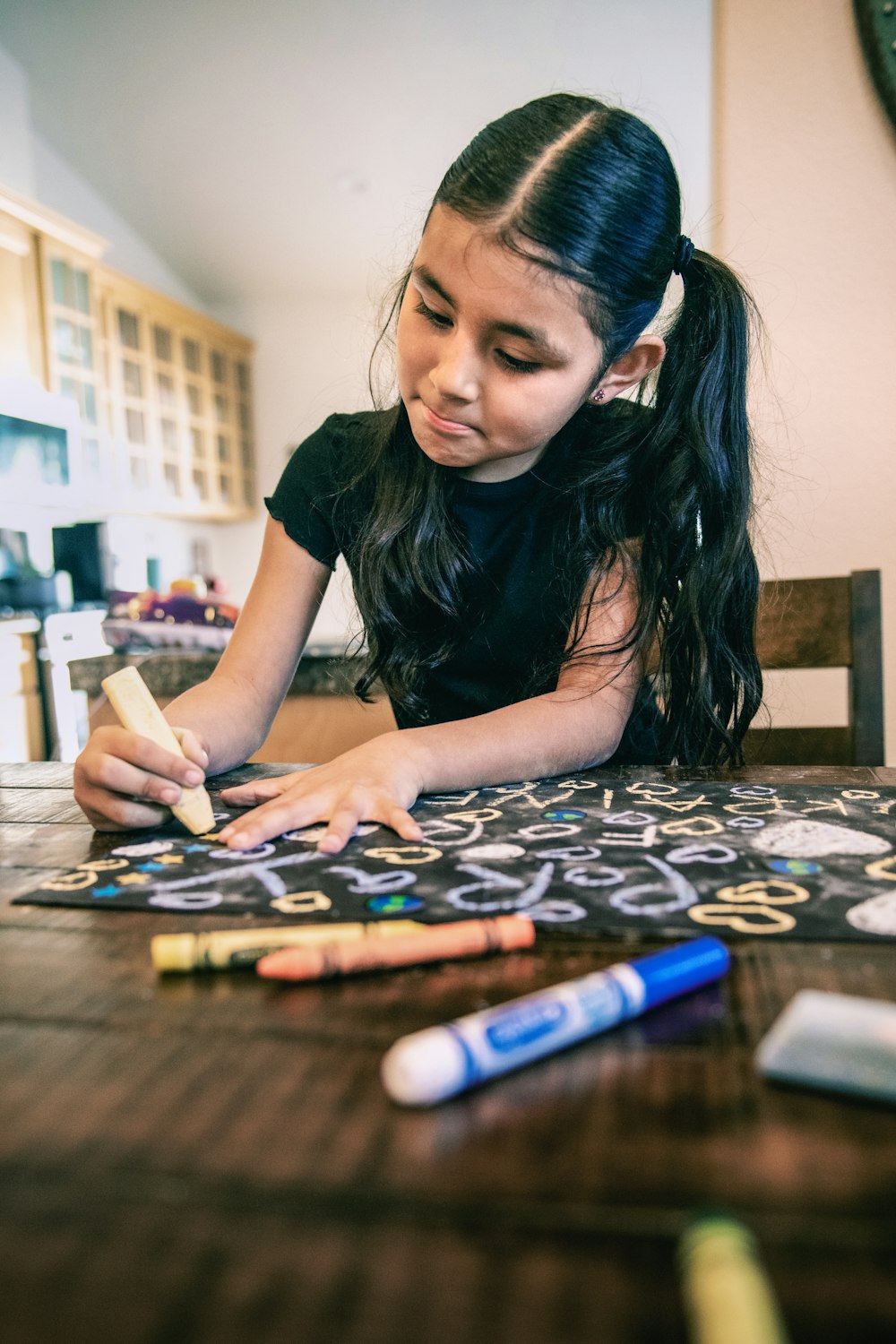 a young girl sitting at a table with crayons on it