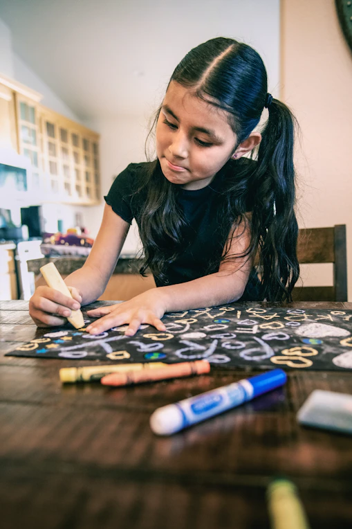 a young girl sitting at a table with crayons on it