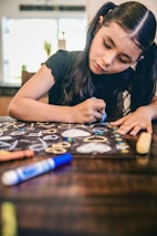 a young girl sitting at a table drawing with crayons