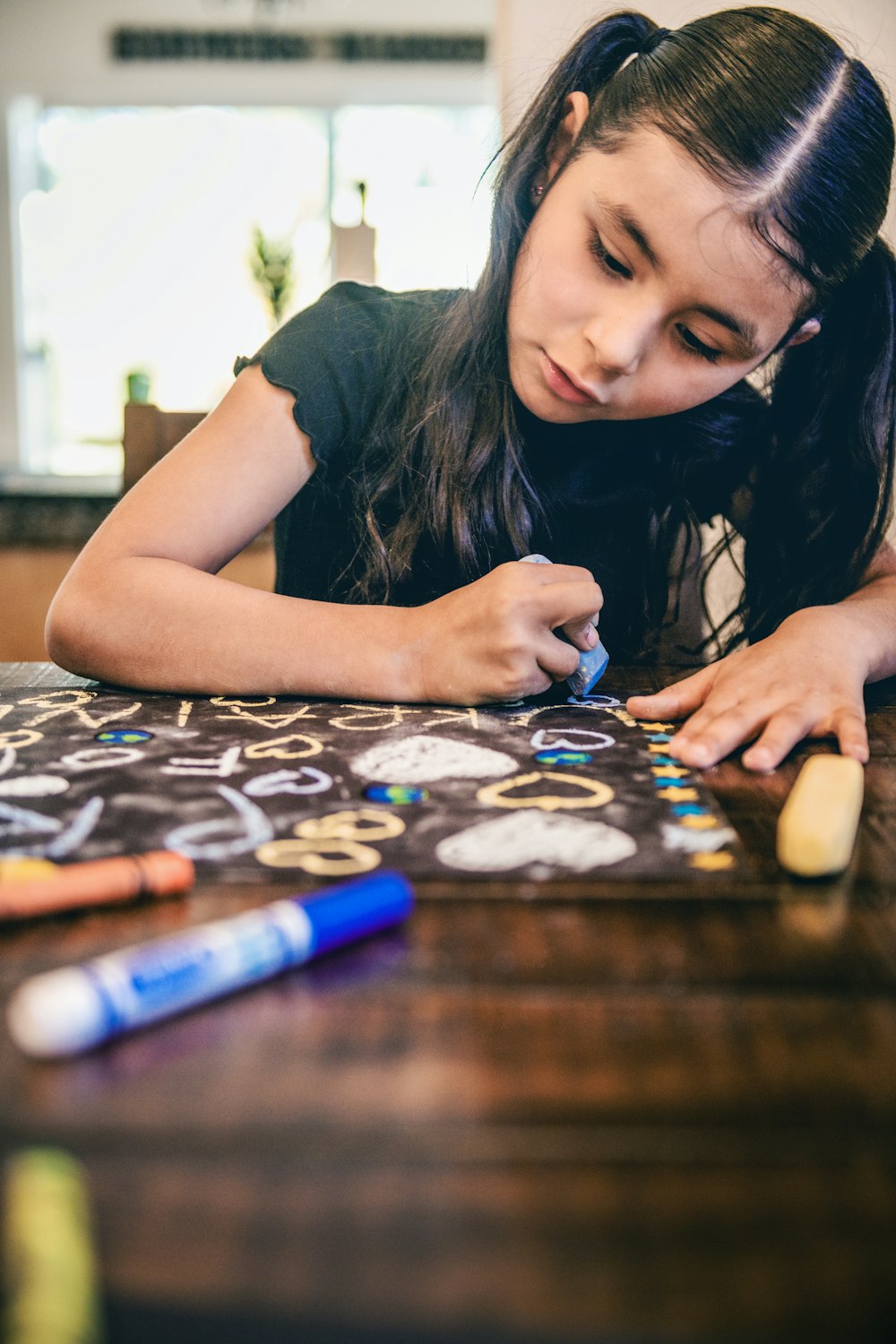 a young girl sitting at a table drawing with crayons