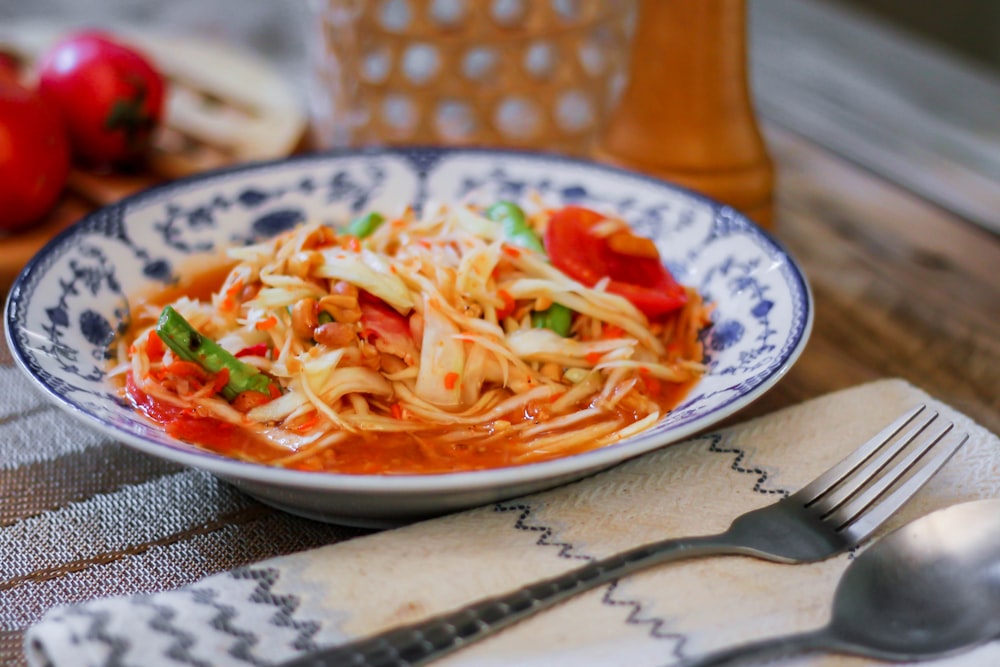 a white and blue bowl filled with pasta and vegetables