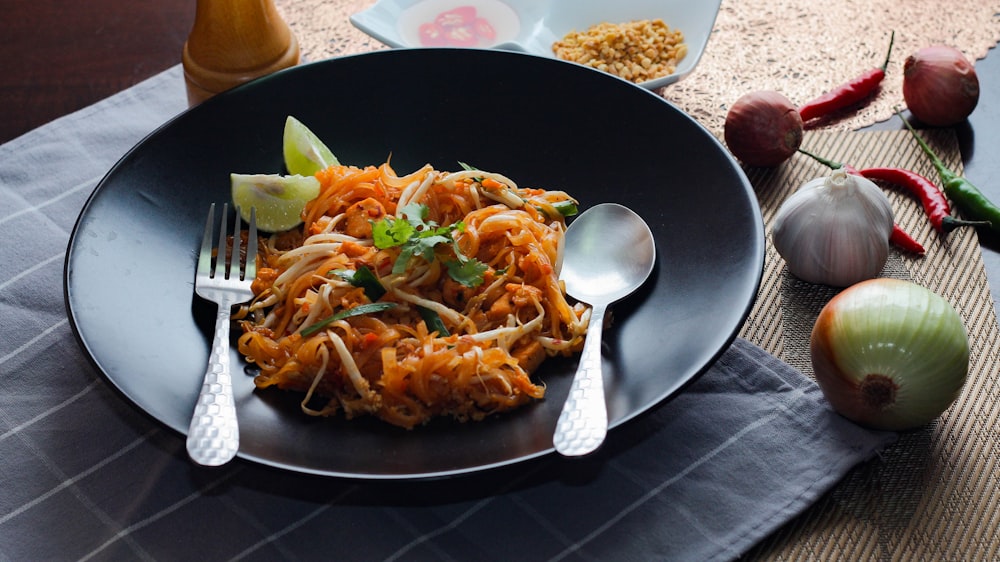 a black plate topped with pasta and vegetables