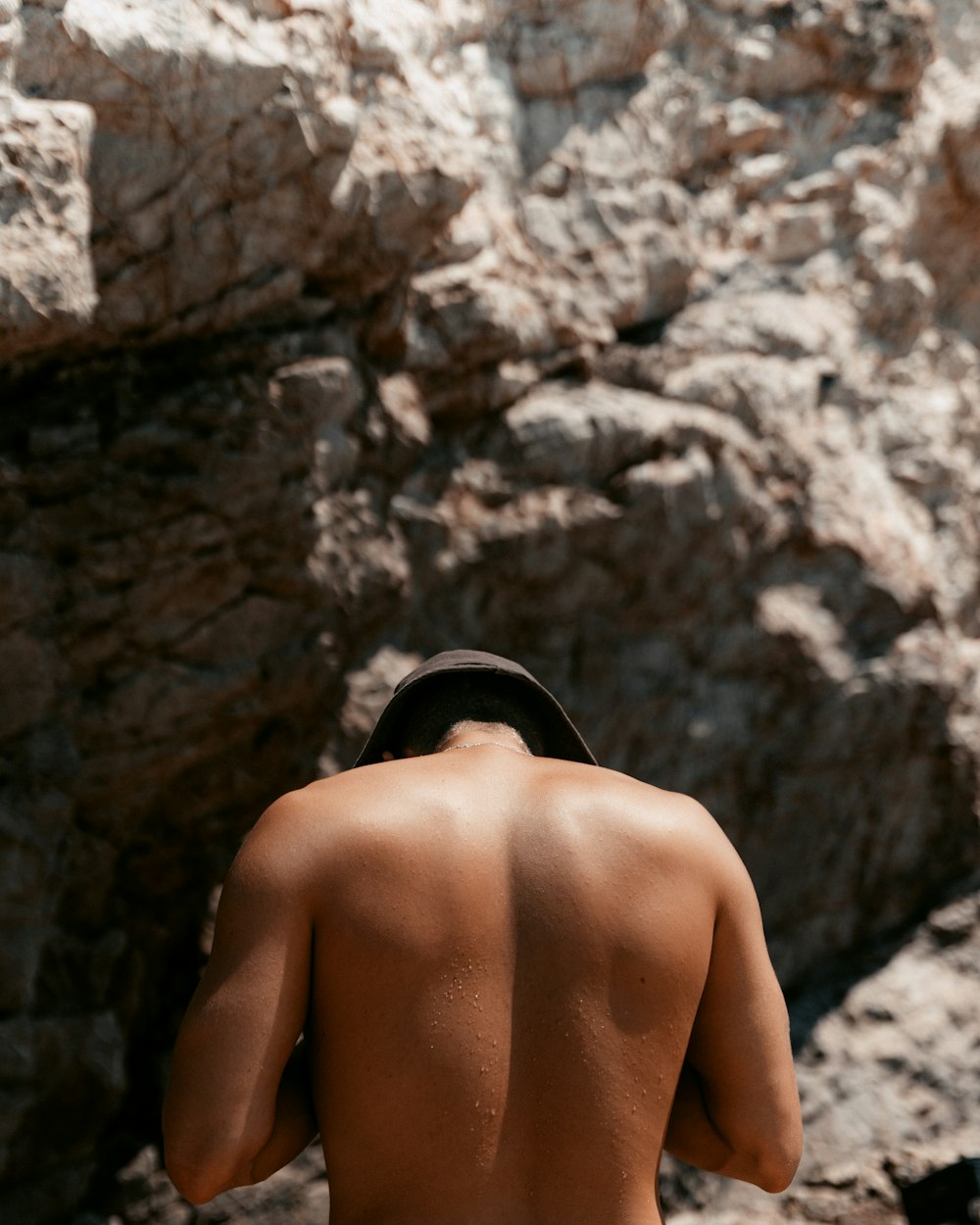 a man with no shirt standing in front of a rock