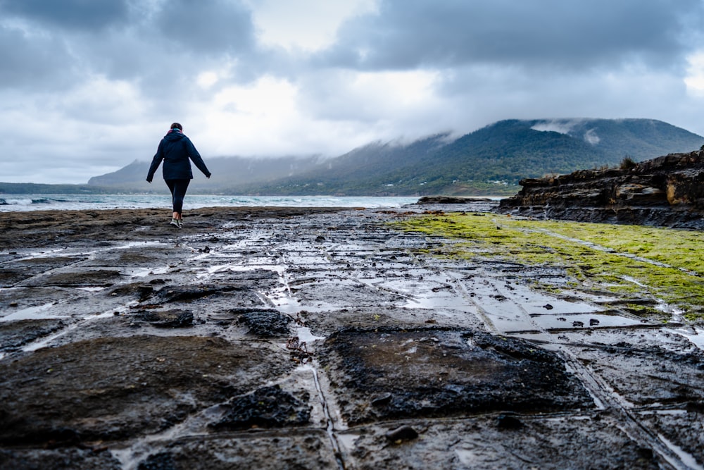 Una persona che cammina su una spiaggia rocciosa vicino a uno specchio d'acqua