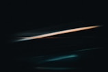Dark abstract art with streaks of turquoise and orange light against a black background, creating a dynamic and mysterious effect.