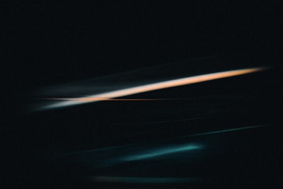 Dark abstract art with streaks of turquoise and orange light against a black background, creating a dynamic and mysterious effect.