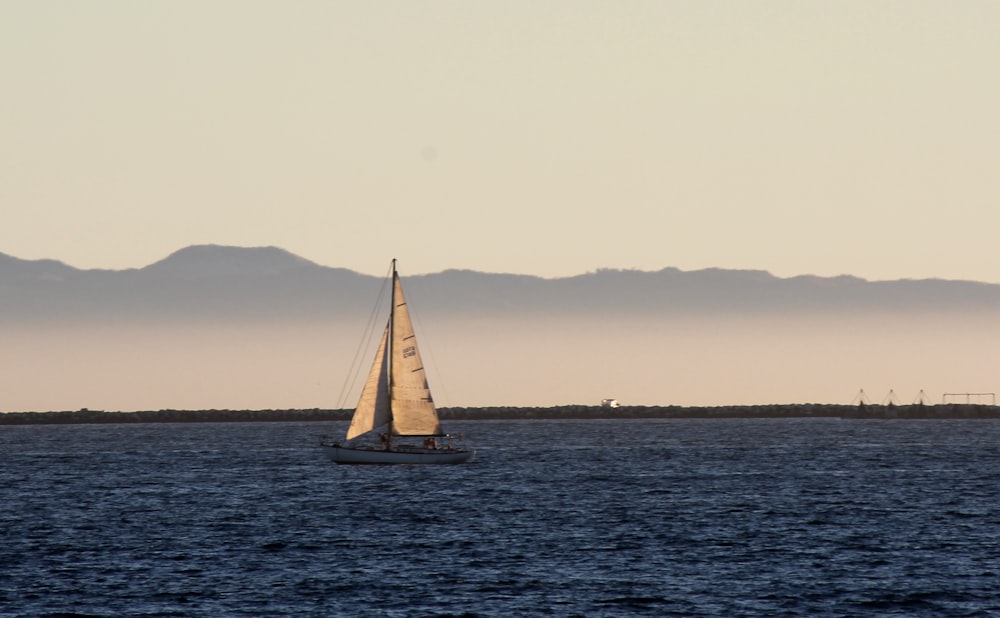 a sailboat in the ocean with mountains in the background