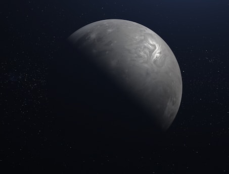 A planet with a swirling cloud pattern on its surface is partially illuminated against the dark backdrop of space. One side is in shadow, highlighting the curve of the celestial body.