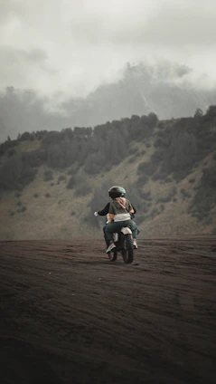 A fierce female biker with flaming skull helmet riding through a dark, fiery landscape.
