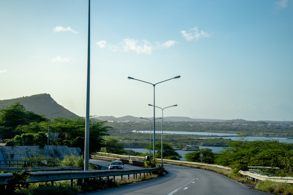 a car driving down a road next to a lush green hillside