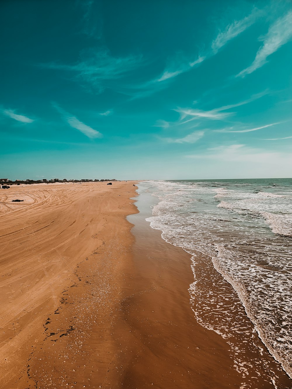 a sandy beach next to the ocean under a blue sky