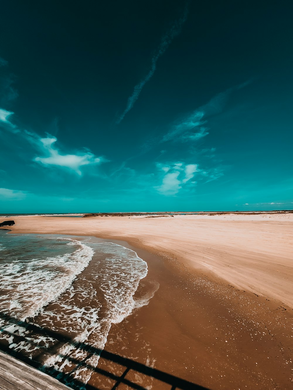 a sandy beach with a wooden walkway leading to the water