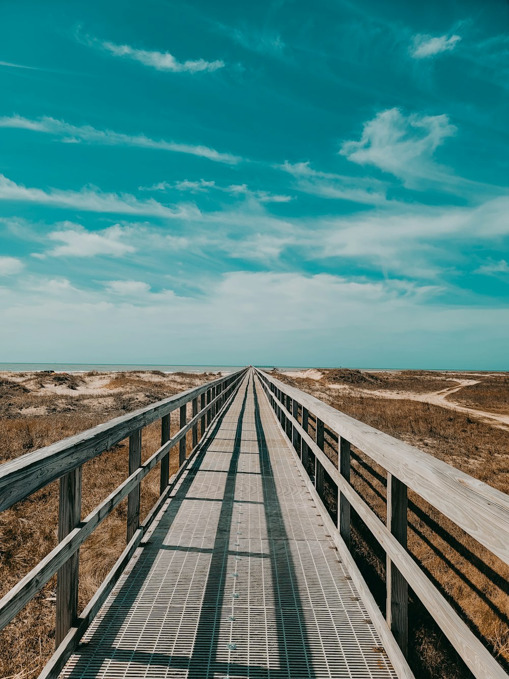 a wooden bridge over a sandy beach under a blue sky