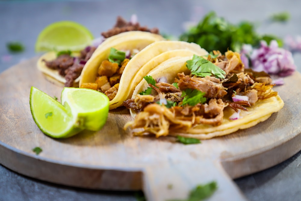 Un plato de madera cubierto con tres tacos y una lima