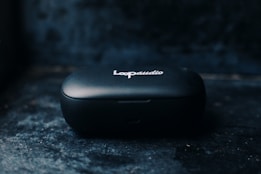 A small, black portable device case with the inscription 'Loop audio' on top, positioned against a dark and slightly textured background.