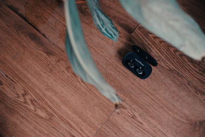 A sleek wireless earbud case open on a marble surface with green plant leaves nearby.