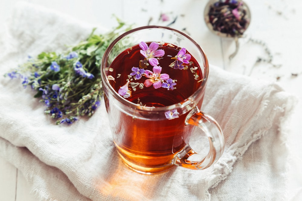 a glass mug filled with tea next to a bunch of flowers