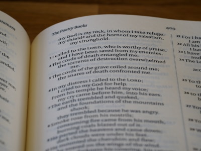 The photograph features an open book displaying text from a religious scripture. The visible pages include chapter numbers and a poetic excerpt about seeking refuge and divine protection. The script is neatly printed in a serif font, and portions of the text are bold for emphasis.