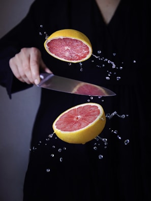 a person cutting a grapefruit with a knife
