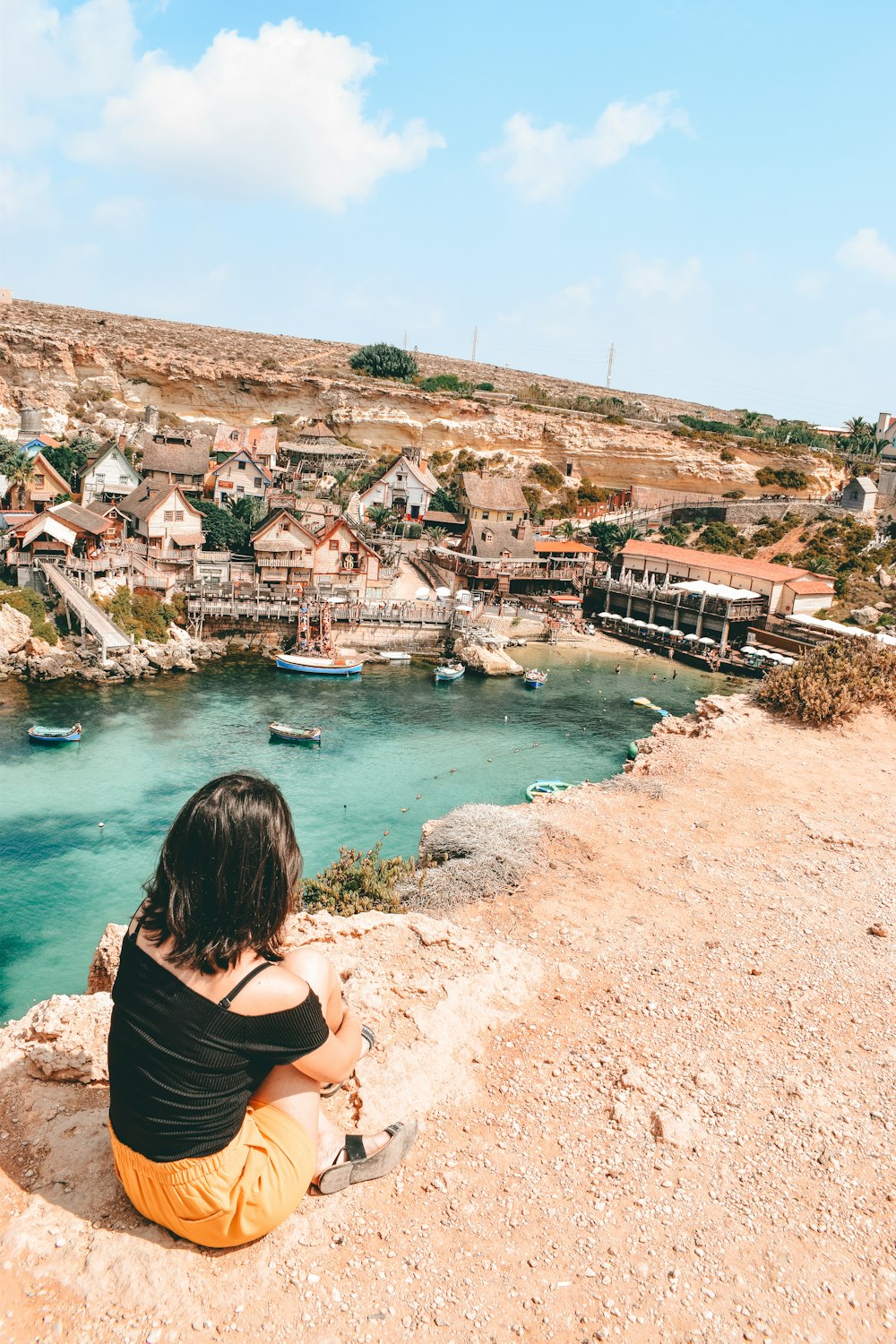 a woman sitting on a cliff looking at the water