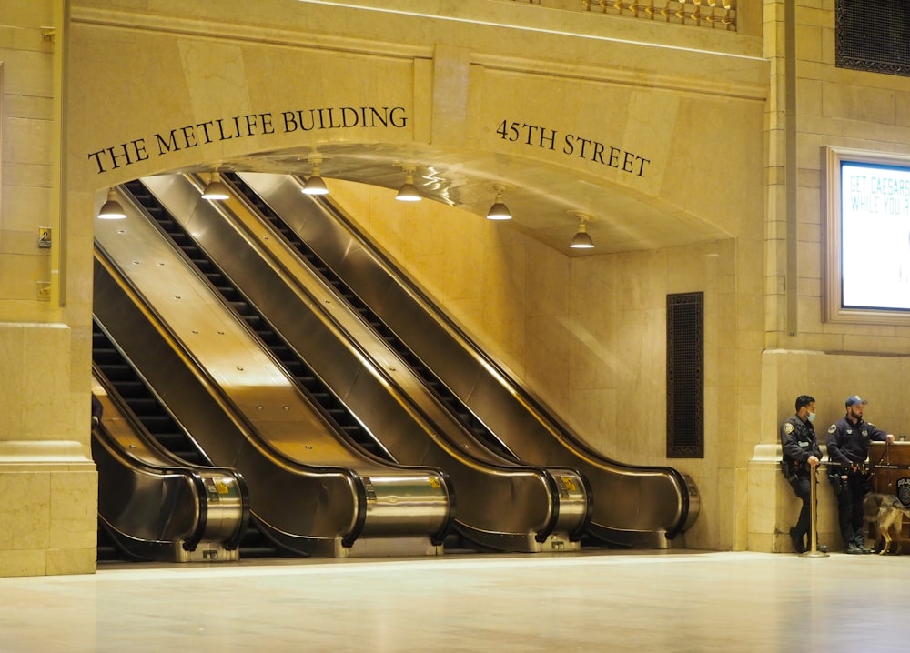 a group of people standing in front of a building with escalators