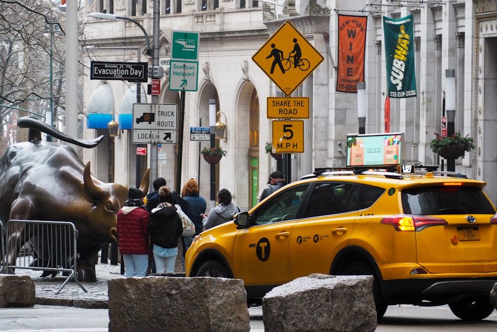 a yellow taxi driving down a street next to a bull statue