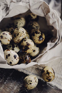 Close-up of fresh quail eggs nestled in straw on a rustic wooden table.