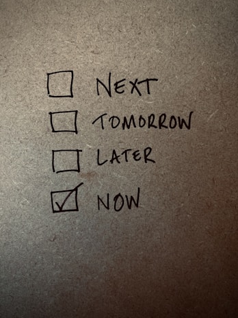 A handwritten checklist on a textured surface with four items labeled 'Next', 'Tomorrow', 'Later', and 'Now', with 'Now' being checked.