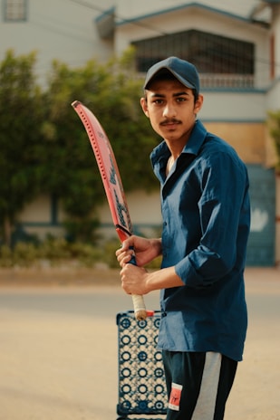 A smiling young man in a baseball uniform holding a bat, standing on a baseball field.