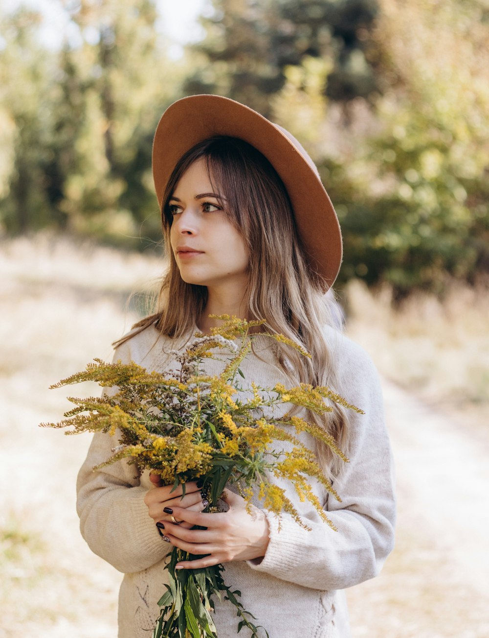 a woman wearing a hat holding a bouquet of flowers